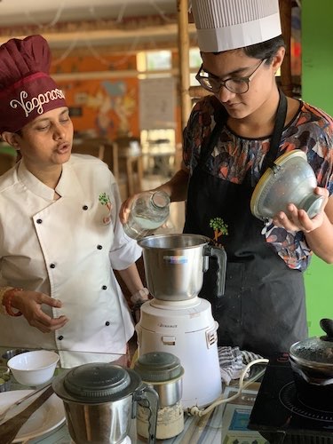 Chef Susmitha with student. They're looking into a steel blender jar. Vegan dairy alternatives class.