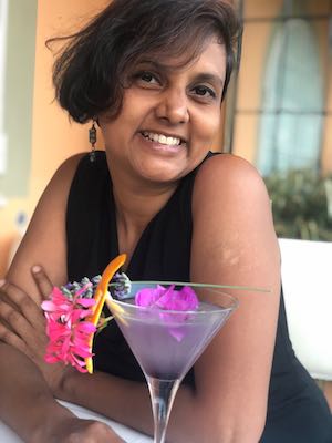 Vegan business coach from India, Susmitha Veganosaurus, seated at a table and smiling at the camera with a fruity drink in front of her.