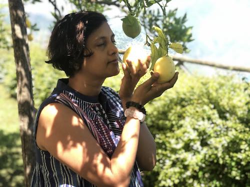Side view of Susmitha Veganosaurus smelling lemons on a tree. Eyes closed, face tilted upwards.