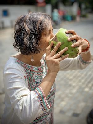 Susmitha drinking tender coconut water straight from the coconut, without a straw.