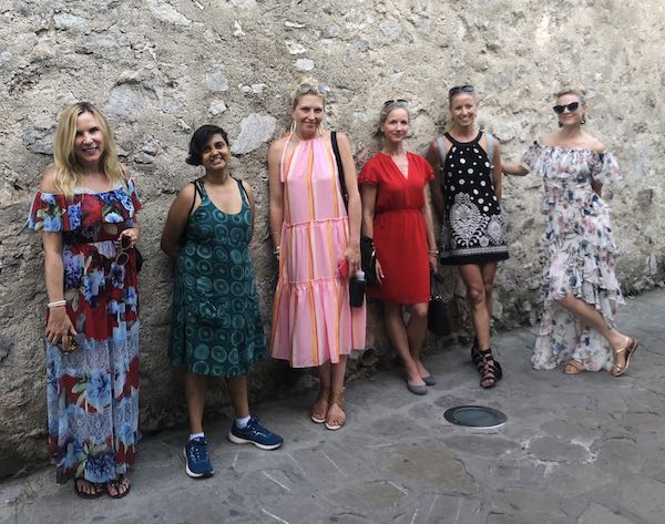 Five women in colourful dresses, standing in front of a wall at Ravello town.