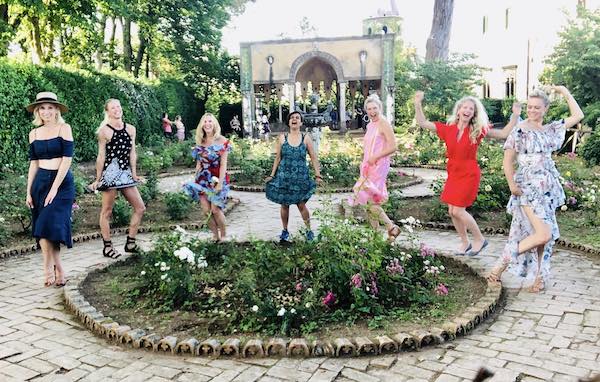 Seven women laughing and dancing in a garden at Villa Cimbrone, Italy.