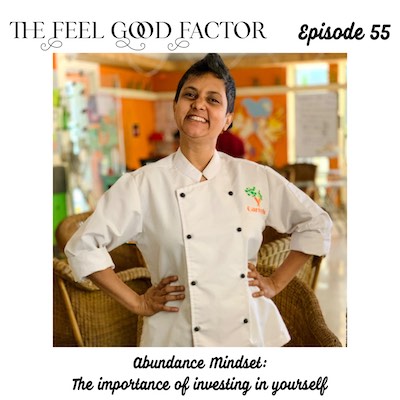 The Feel Good Factor, episode 55. Susmitha Veganosaurus, Indian lady with super short haircut, wearing a chef coat, smiling wide at the camera with hands on hips. Blurred background. Abundance Mindset: The importance of investing in yourself