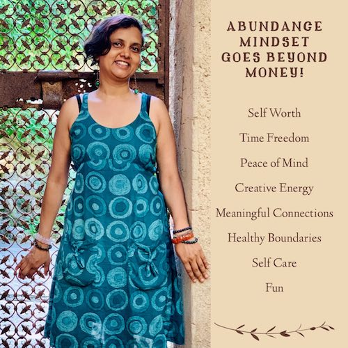 Susmitha in an aqua dress, smiling, with back against a rusty grill. On the right is the text: Abundance Mindset Goes Beyond Money. Self Worth, Time Freedom, Peace of Mind, Creative Energy, Meaningful Connections, Healthy Boundaries, Self Care, Fun.