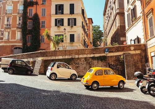 Cobbled street in Rome. Cute retro cars parked on the side. Old buildings in the background.