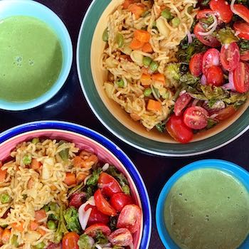 Bowls of veggie loaded noodles an cherry tomato salad with mugs of kale soup on the side. Photo captured from above. Black background.