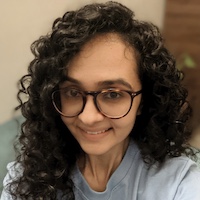 Close up headshot of Shruti Mishra, young Indian woman with lovely curls. Wearing glasses and smiling at the camera.