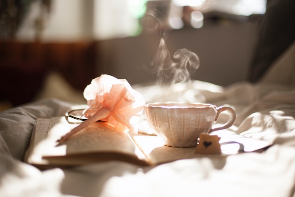 Close up side view of an open book on a bed with a flowery pen and dainty tea cup on it. A world before smart phone addiction.