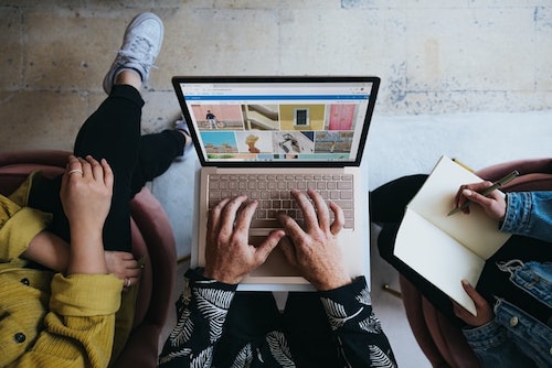 Top view on three people. Only hands and legs seen. Middle person has a laptp on their lap. Person on the right has an open notebook, with a pen poised to write. Building a healthy business relationship.