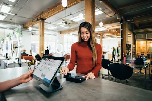 Smiling woman swiping her card at a billing counter in a cafe