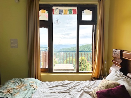 A bright, cozy bedroom. Bed next to a window with a beautiful view of the mountains and sky.