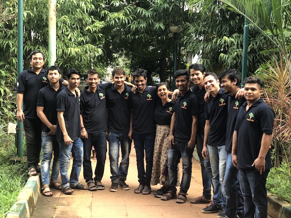 Legendary Carrots Restaurant Team. Indian people (one short woman and eleven young men) in dark blue polo shirts (uniform) standing in a park with their arms around each other's shoulders.