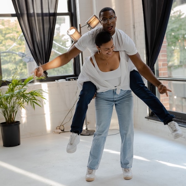 Black woman lifting up a black man on her back. Both are smiling. Windows, curtains, plants in the background. Piggy back a new habit on an existing one.