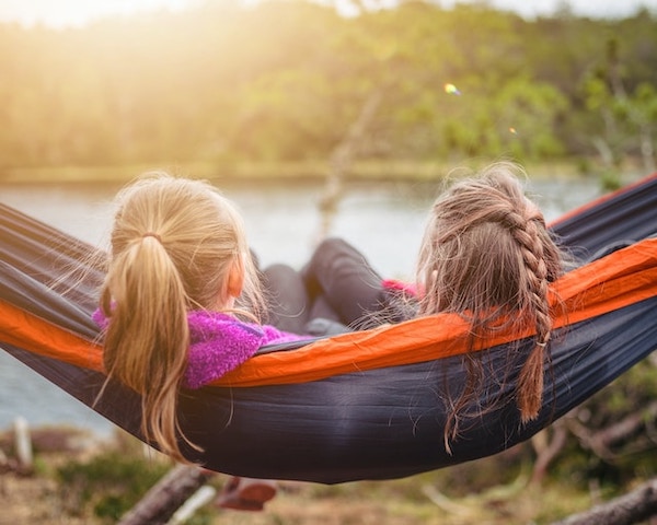 Two little girls sitting in a hammock, facing away from us, looking at a lake. They seem completely relaxed and chilled out, with no agenda.