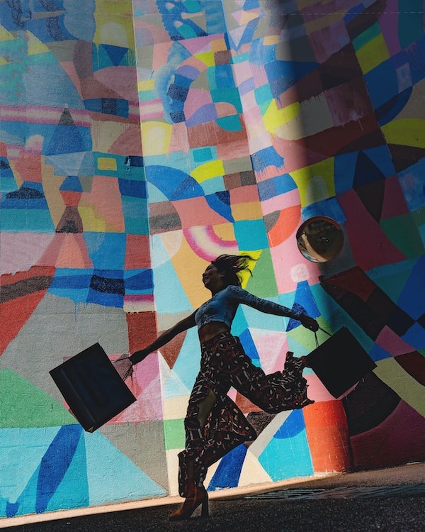 Silhouette of woman skipping along a colourful, painted wall mural with shopping bags in hands.