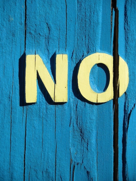 NO painted in large, bold letters in yellow paint on a blue wooden wall.