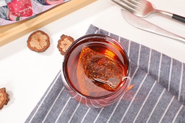 Glass cup with perfectly brewed Rooibos tea. Teabag can be seen. Pretty table setting all around.