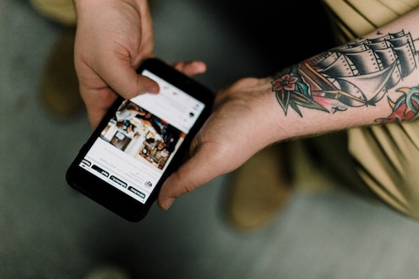 Tattooed hands holding a mobile phone and scrolling. Information overconsumption.