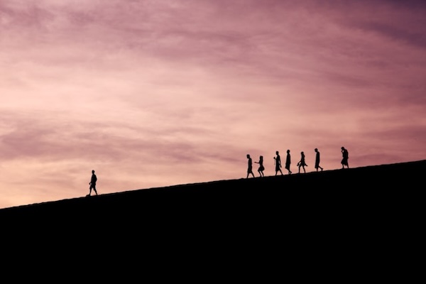 Silhouette of mountain slope. One person walking away from a group.