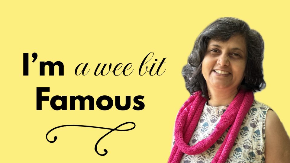 Susmitha S – vegan chef, holistic business coach, multi-passionate creator and teacher – wearing a white dress with aqua prints and a bright pink knitted infinity scarf. Smiling at the camera. Text on bright yellow background: I'm a wee bit famous. Veganosaurus.