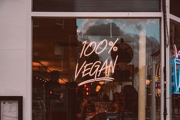 Sign on a glass window of a vegan cafe 100% Vegan. I'll help you build and grow your vegan business joyfully.