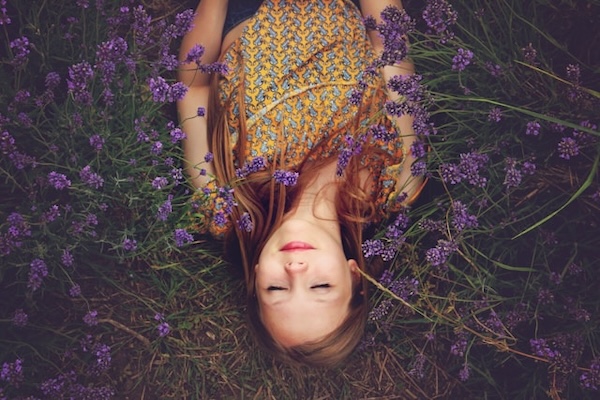 Glowing young woman asleep peacefully among purple flowers. She has a peaceful expression.