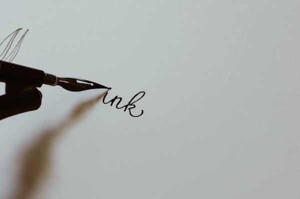 White sheet of paper with the word "ink" written in black ink pen. Writing with our hand, pen to paper, is so much better than typing.