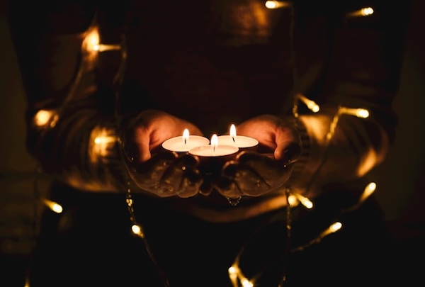 Person holding tealight candles glowing in their open palms. String lights glowing all around their arms. Let the light flow through you and free-write the channeled message onto the page.