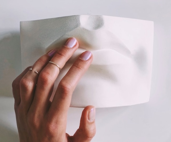 Hand gently touching sculpture of a mouth. Power of touch to activate the parasympathetic nervous system. Easy and simple morning habit.