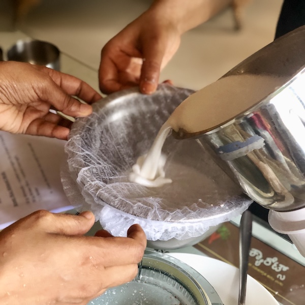 Almond brown rice mylk being poured from a blender jar into a steel bowl through a mesh strainer. How to conduct a vegan cooking class.