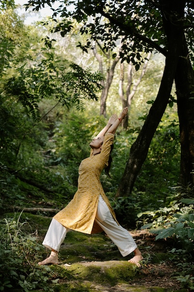 Ekta Minocha of Poornatvam Yoga, holding a yoga pose in the middle of a lush, green forest path.