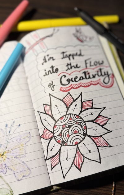 Ruled notebook with simple doodles and an affirmation: I'm tapped into the flow of creativity.